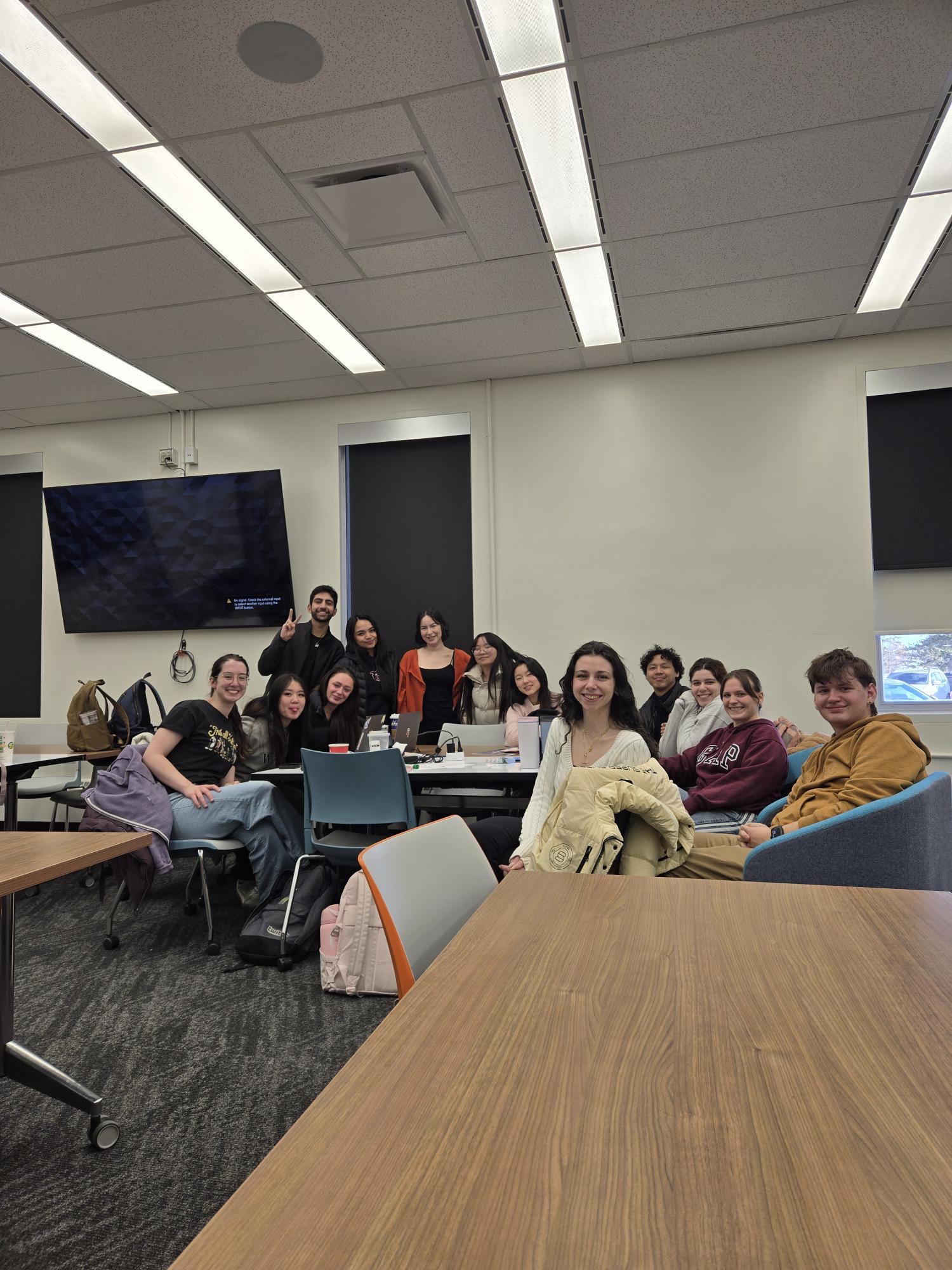 Thirteen students gathered at a table on SAIT campus, smiling at the photographer
