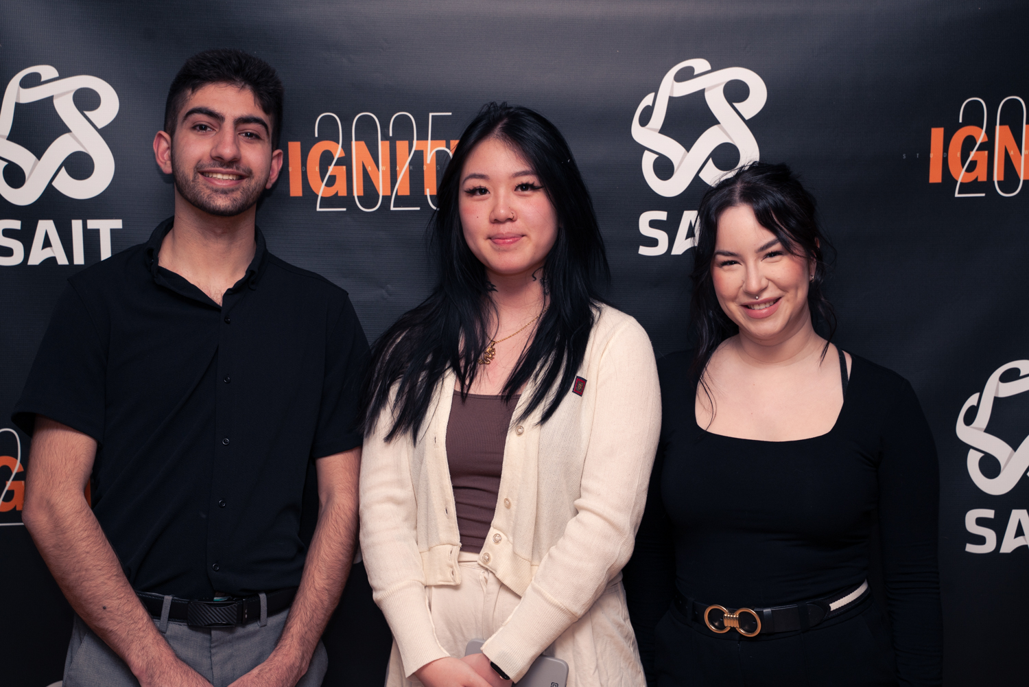 Moe, Wing, and Robyn smiling as they stand in front of a dark backdrop that reads SAIT Ignite 2025